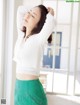 A woman in a white sweater and green skirt posing for a picture.