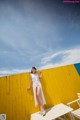 A woman in a white dress standing on a wooden bench.