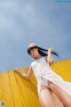 A woman in a white dress leaning against a yellow wall.