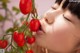 A woman smelling a bunch of red tomatoes on a plant.