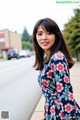 A woman in a floral dress standing on the side of a road.