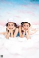 Two young girls laying on top of a fluffy white cloud.