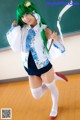 A woman with green hair holding a scythe in front of a blackboard.