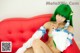 A woman with green hair sitting on a red couch.