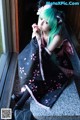 A woman with green hair sitting on a window sill.