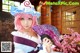 A woman in a pink wig holding a purple fan.