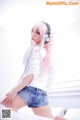 A woman with pink hair wearing headphones on a bed.