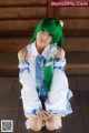 A woman with green hair sitting on a wooden floor.
