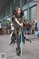 A woman dressed in a black and gold outfit holding a sword.