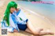 A woman with green hair sitting on a beach.