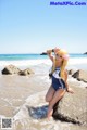 A woman in a bathing suit sitting on a rock on the beach.