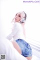 A woman with pink hair wearing headphones sitting on a bed.