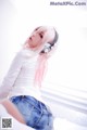 A woman with pink hair wearing headphones sitting on a bed.