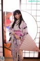 A woman in a kimono holding a fan in front of a window.