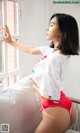 A woman in a white shirt and red shorts leaning against a window.