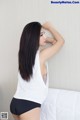 A woman in a white tank top and black shorts posing on a bed.