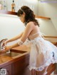 A woman in a white dress is washing her hands in a kitchen sink.