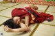 A woman in a red kimono laying on a tatami mat.