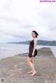 A woman in a black dress standing on a pier by the ocean.