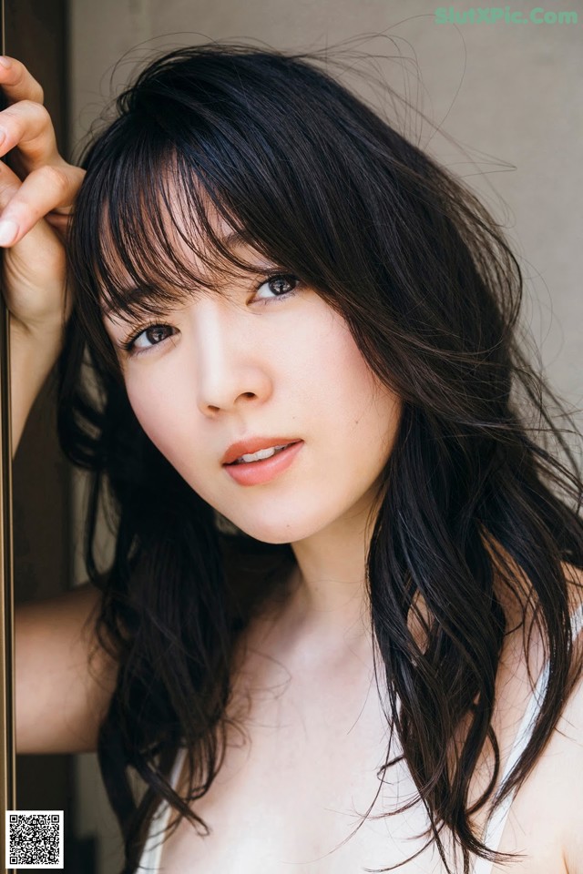 A woman with long black hair leaning against a wall.