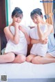 Two young women sitting on a bed with pillows.