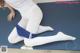 A woman in white tights and a white shirt is sitting on a blue mat.