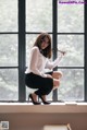 A woman in a white shirt and black skirt sitting on a window sill.