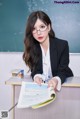 A woman sitting at a desk in front of a blackboard.