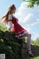 A woman in a red and white dress sitting on a stone wall.