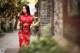 A woman in a red cheongsam leaning against a brick wall.